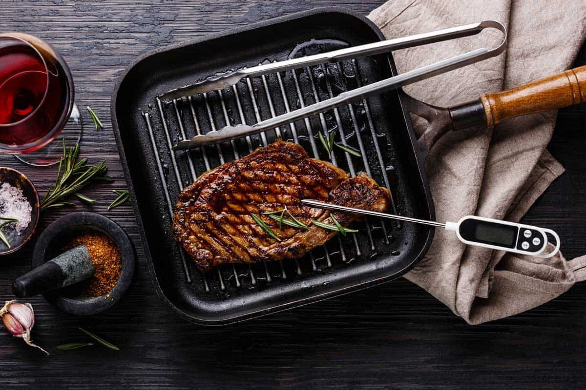 锅上烤西冷牛排和肉类温度计在黑色烧木背景,8种烹饪温度计你可能需要