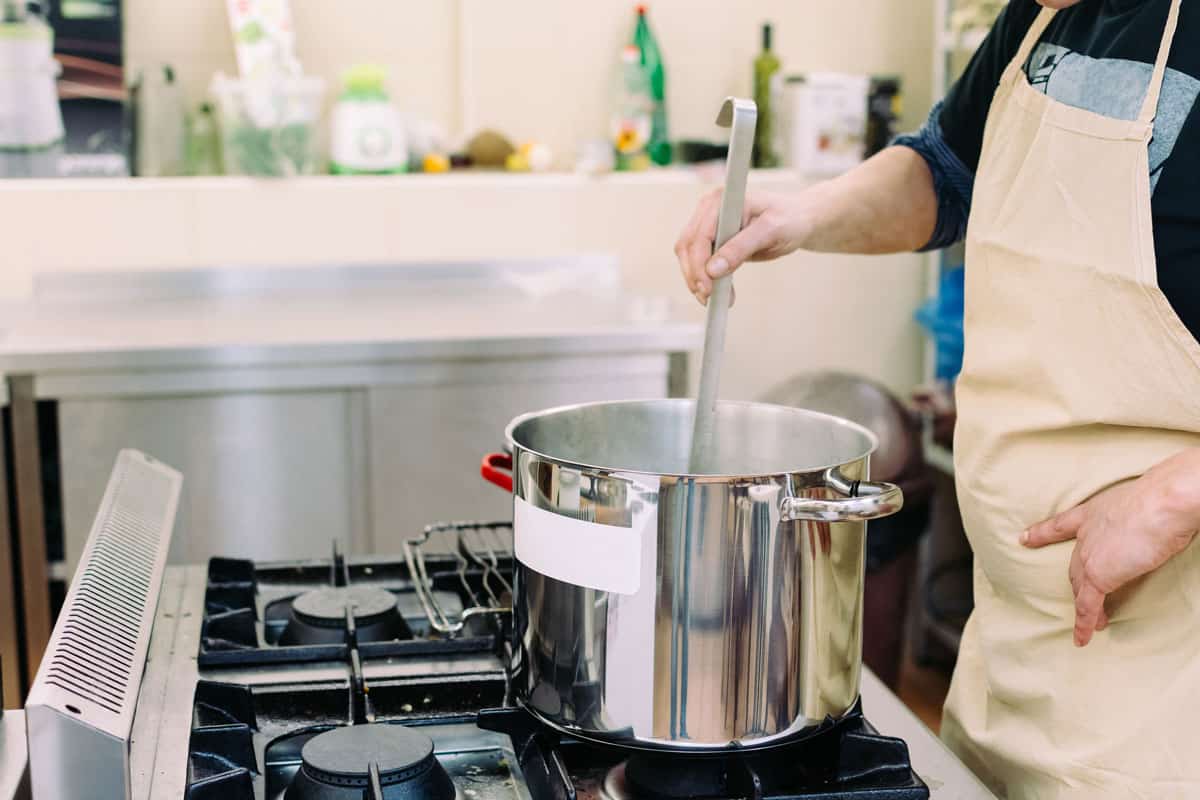 女子拿着炊具，在她的四燃烧器煤气炉上的汤锅上做饭，“我能用汤锅煮什么?”