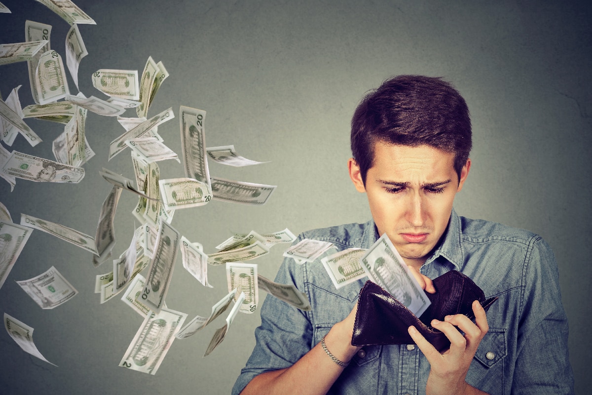 悲伤的男人看着他的钱包里的钱美元钞票飞了出去