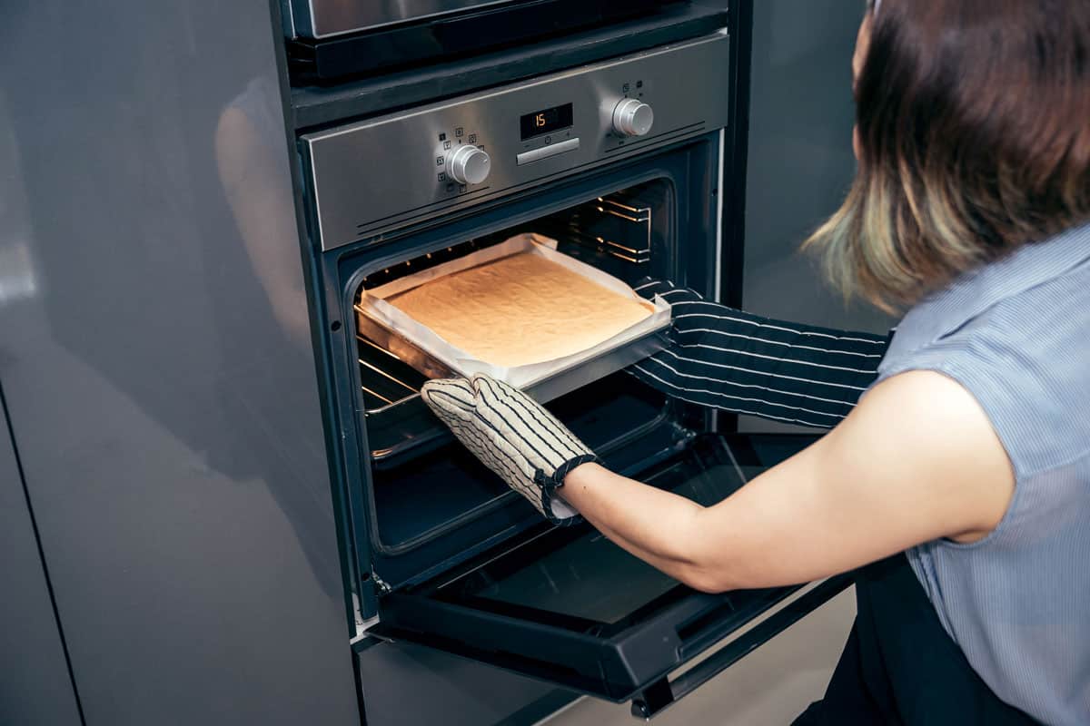 年轻女子拿出一块新鲜出炉的烤蛋糕在烤箱