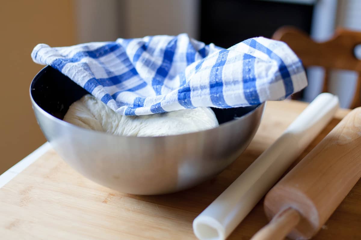 一个混合碗，里面有生饼干面团，上面盖着蓝色条纹布
