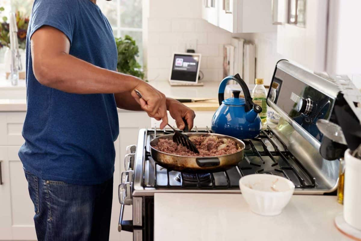 年轻的成年男子站在厨房的灶台上做饭，用锅铲和煎锅雷电竞官网网址
