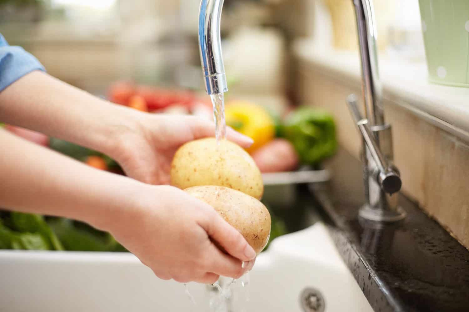 一个女人在厨房的水槽上洗两个土豆雷电竞官网网址