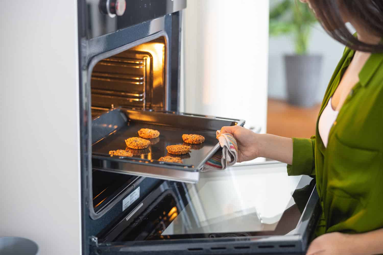 年轻的亚洲家庭主妇打开对流烤箱”width=