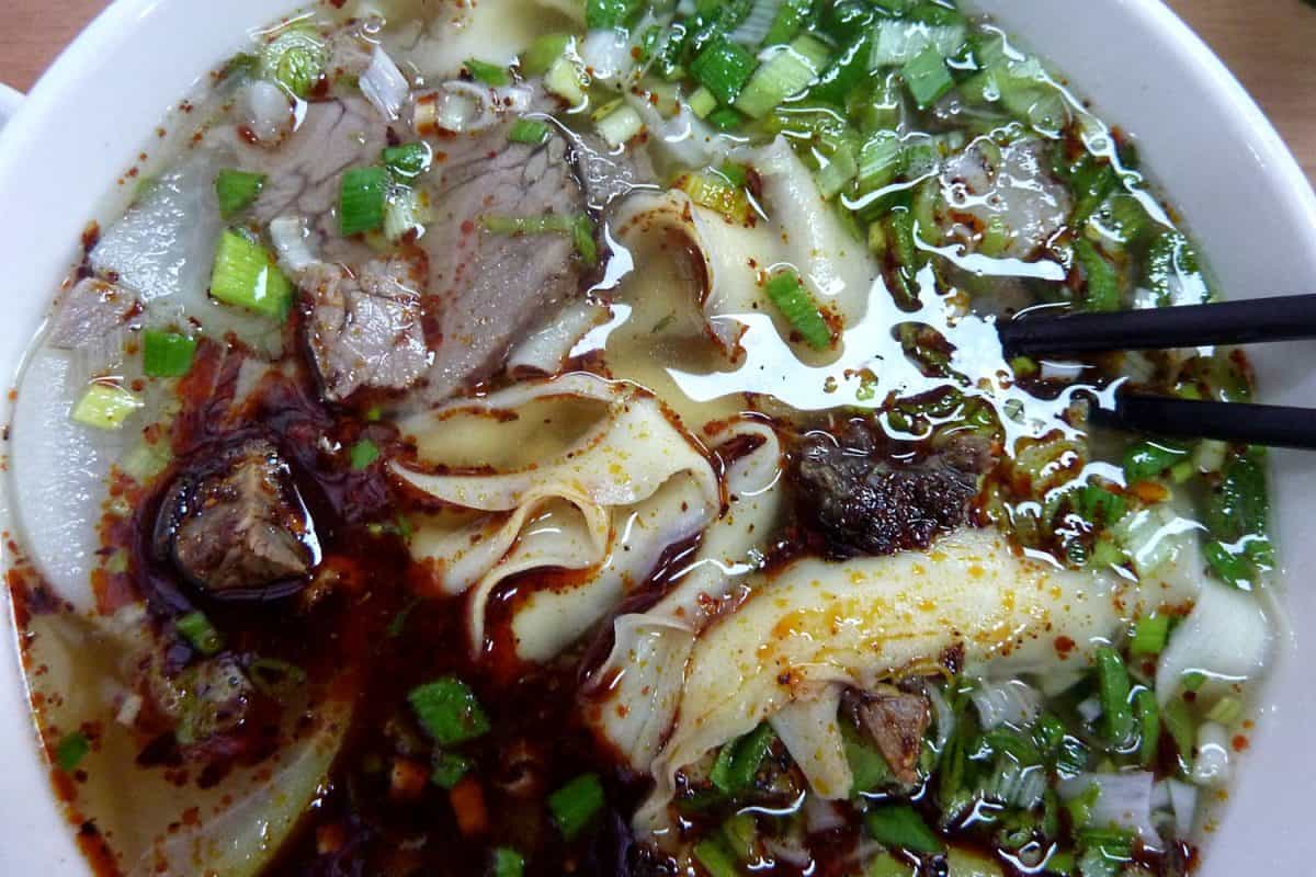 兰州拉面是一种著名的面条，用筷子夹在白色的碗里