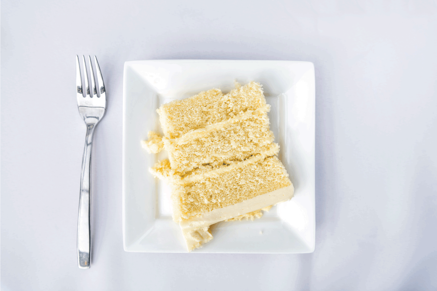 查看下特写餐厅或婚宴白色餐桌桌布一盘香草奶油蛋糕切片，叉子
