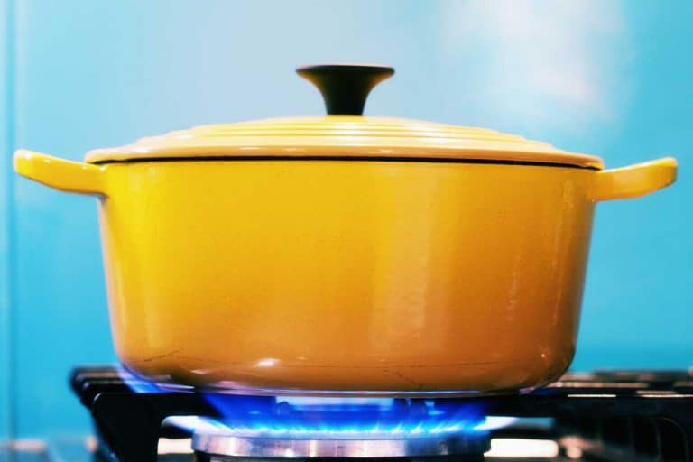 A yellow enamel casserole with its lid on, sits on a lit gas burner creating steam as it heats, Can Le Creuset Ceramic Go On The Stove?