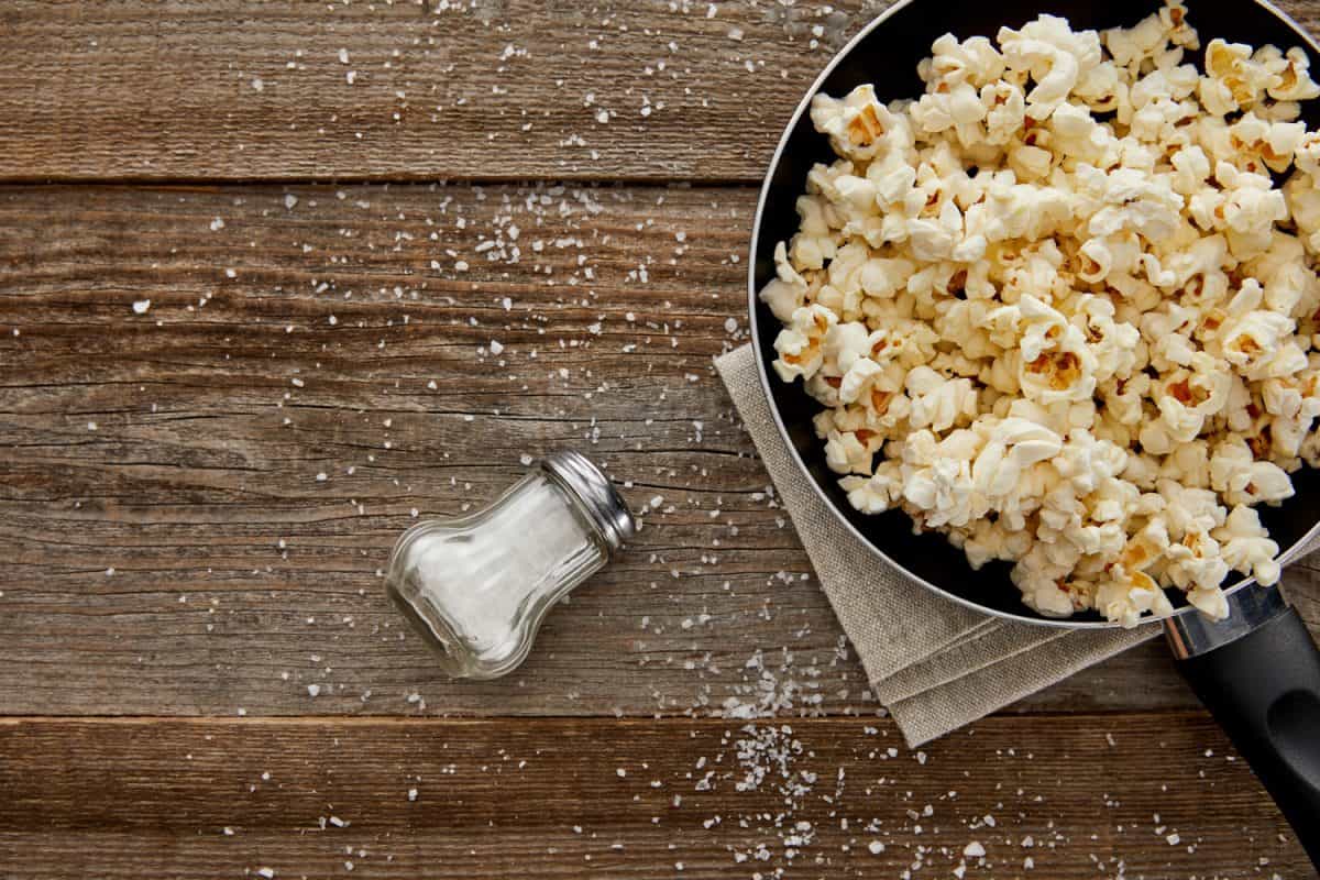 俯视图美味的爆米花在煎锅附近散落的盐在木制背景
