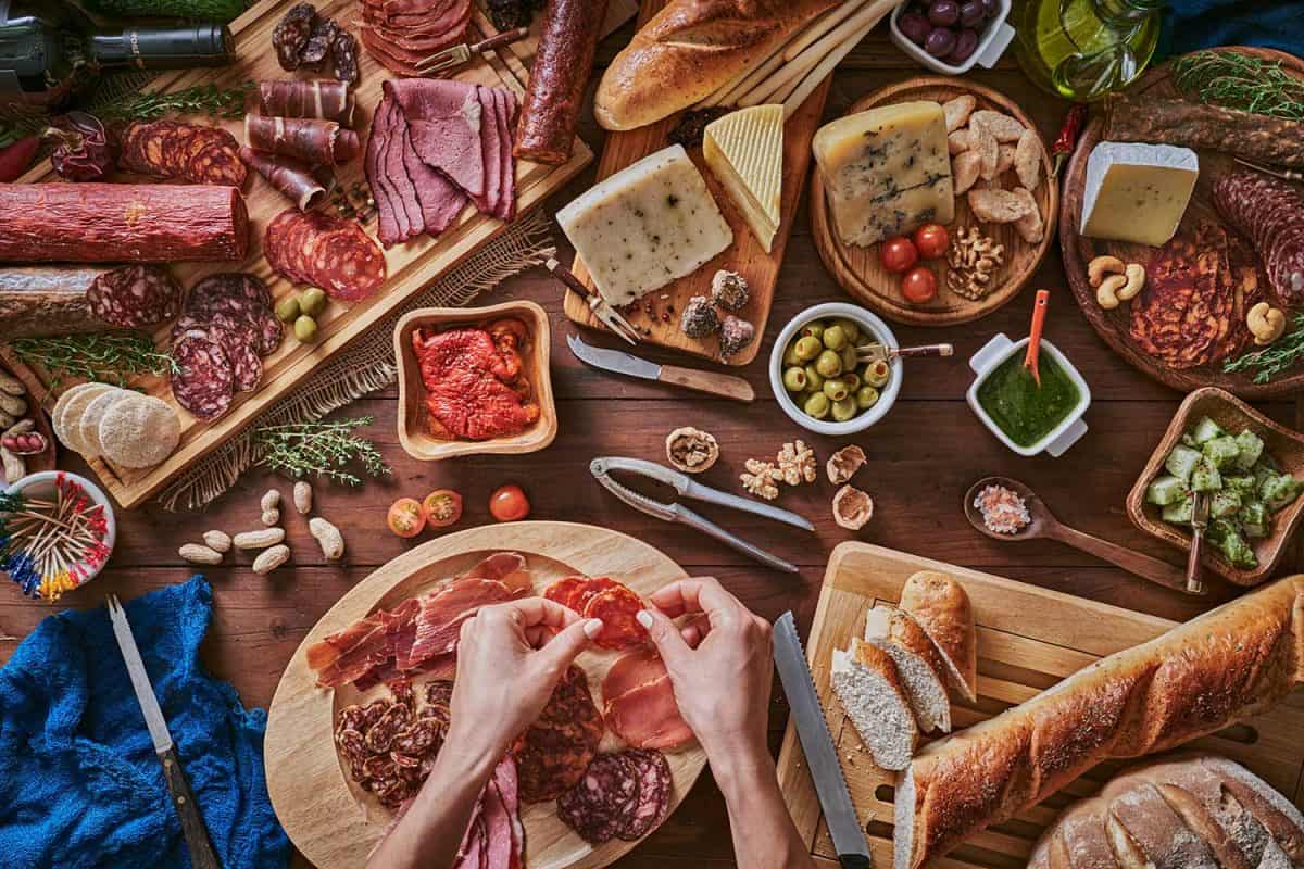 女性的手准备零食和开胃菜在一套充满什锦腌火腿和奶酪在质朴的木头”width=