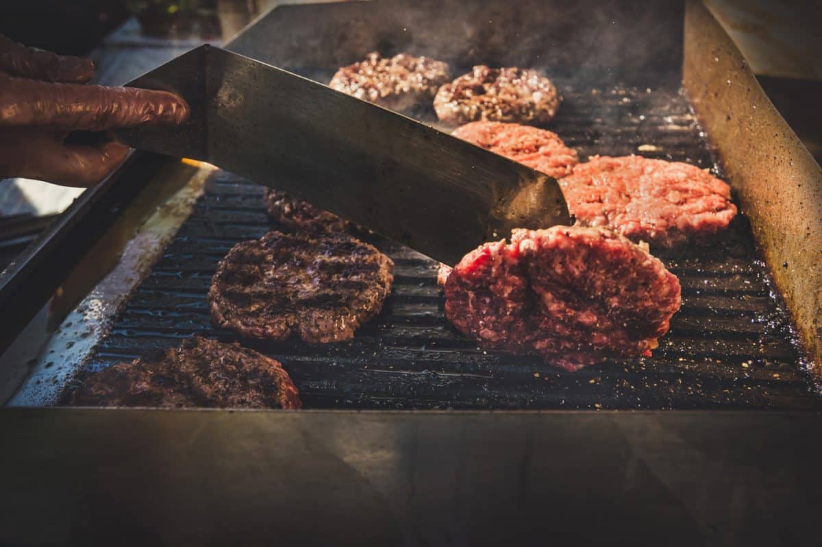 燃烧的烧烤和牛肉汉堡。厨师掀帕蒂用金属铲烧烤