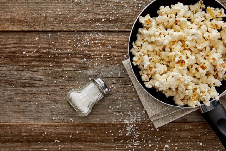 顶视图附近的煎锅中美味的爆米花撒盐在木制背景,10种石油爆米花需要考虑