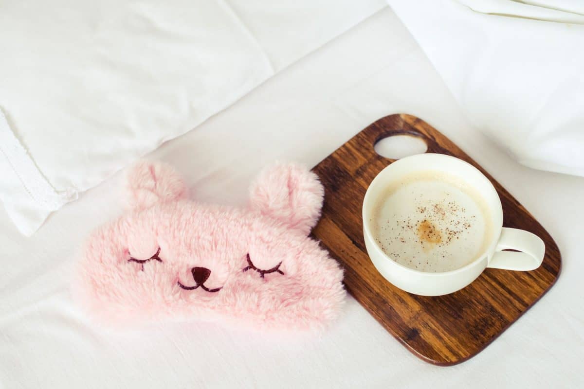 一个装有一杯牛奶和一个小泰迪熊眼罩的木杯垫