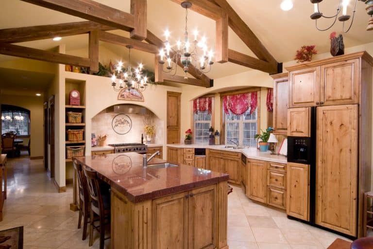 A rustic interior kitchen with bright chandeliers and oak cabinets matching the exposed ceiling membrane, 17 Rustic Kitchen Cabinets Ideas You Should See