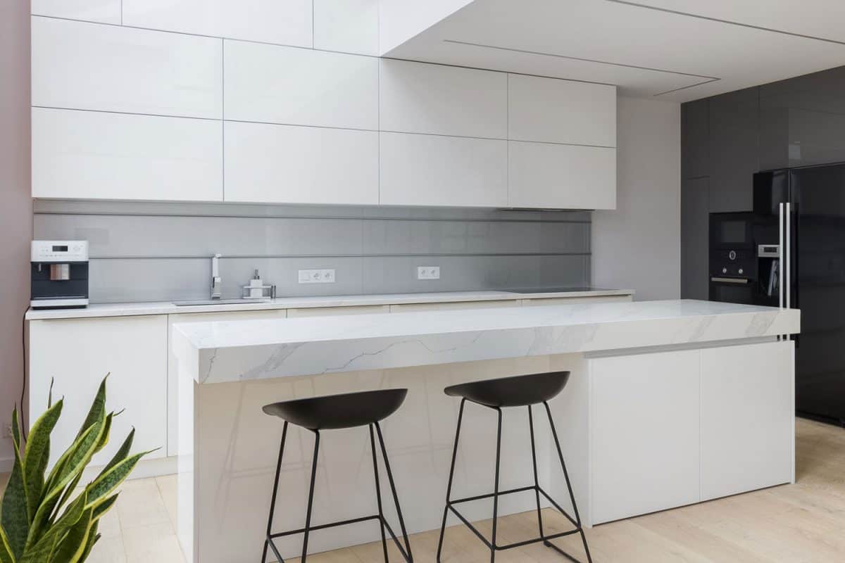 白色风格的厨房，白色台面，黑色雷电竞官网网址吧台凳和白色橱柜
