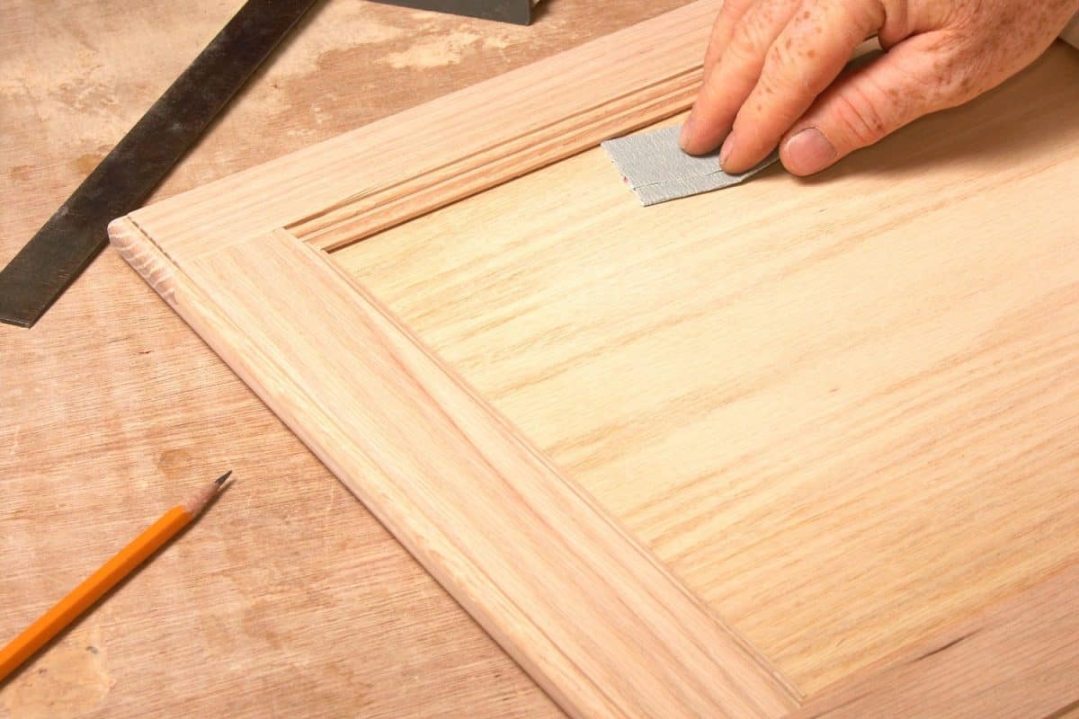 一名工人在给橱柜上漆之前，正在用一小块砂纸