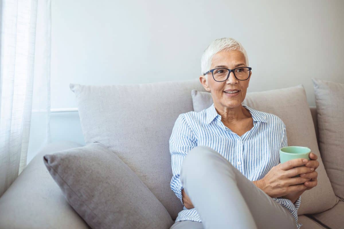 美丽的50岁白人女士坐在沙发上喝茶