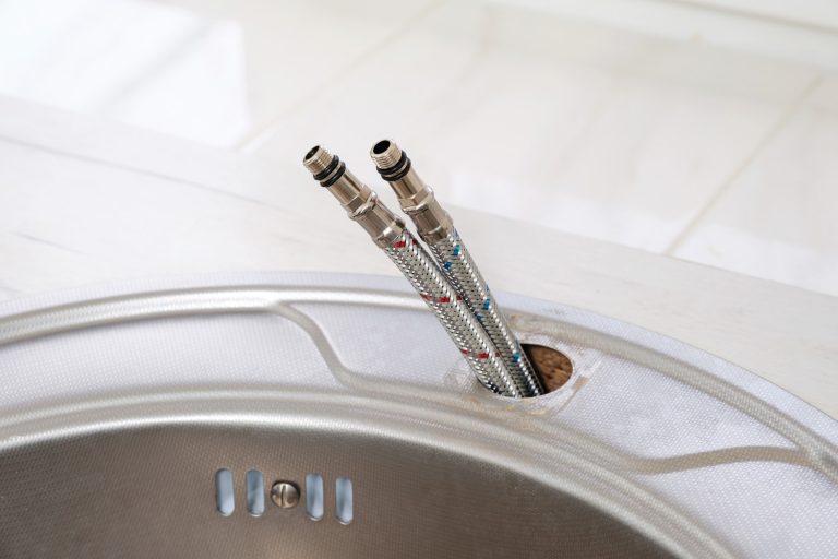 Flexible water hoses for cold and hot water to installation of the kitchen faucet into a sink close-up - Do Kitchen Faucets Come With Hoses