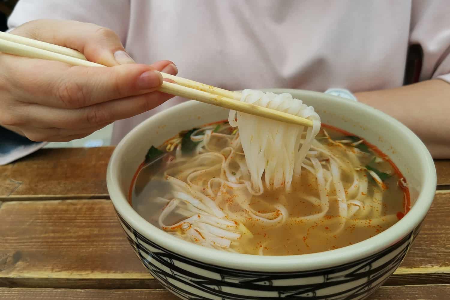 女孩在街头咖啡馆用筷子吃米粉”width=