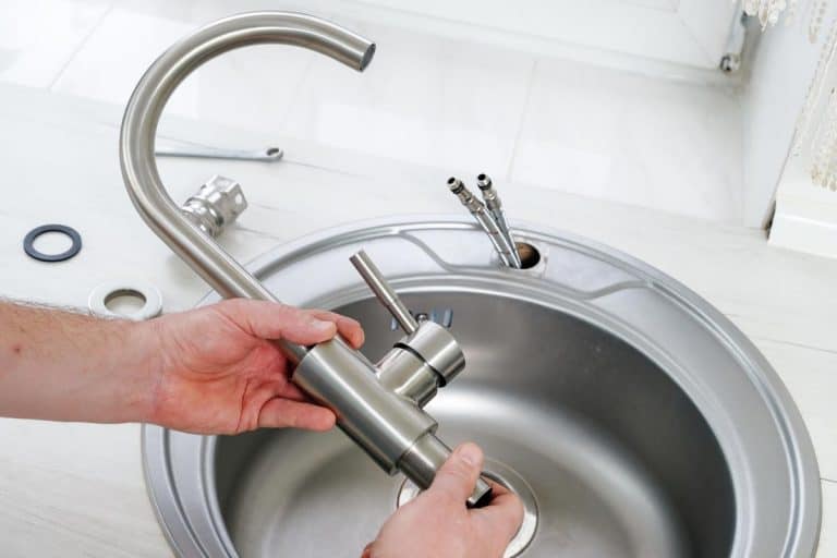 A plumber hand holds a new faucet for installing into the kitchen sink, How Long Does It Take To Replace A Kitchen Faucet