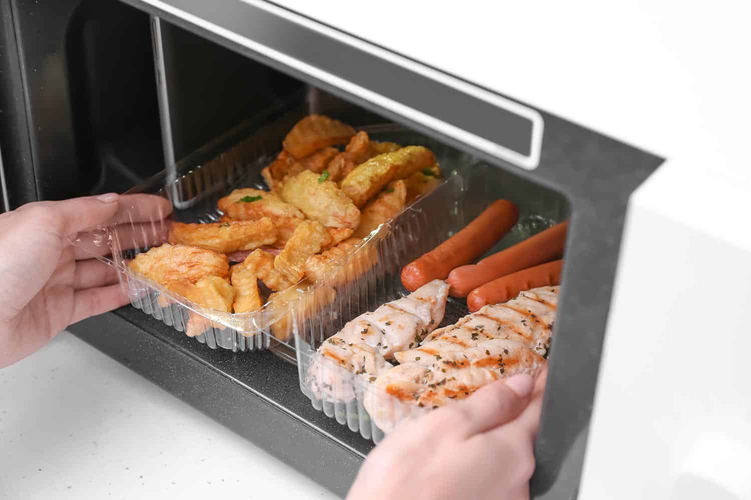 一名妇女将装有炸土豆、鸡肉和香肠的容器放入厨房的微波炉中雷电竞官网网址