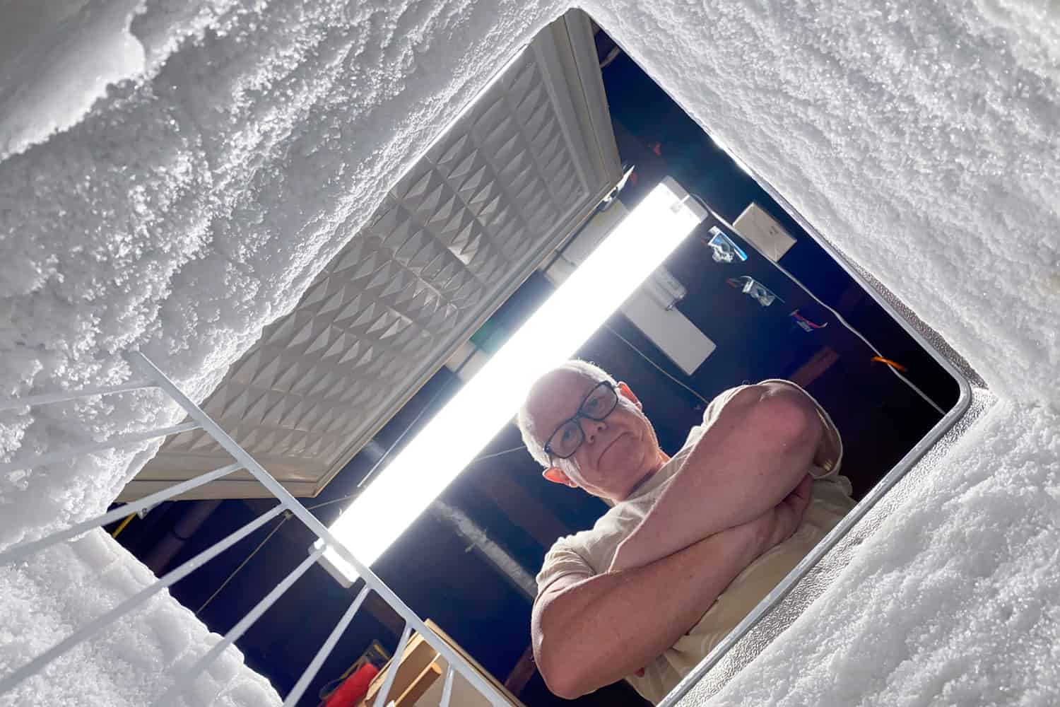 沮丧的男人低头看着冰箱除霜的胸部。