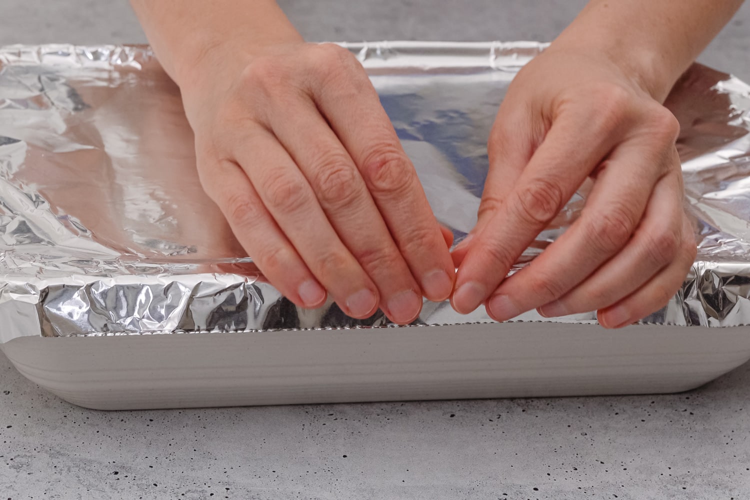 烤盘覆盖铝箔关闭在桌上,前视图,女人的手。菠菜烤宽面条的配方。在烘烤之前用铝箔盖烤宽面条。