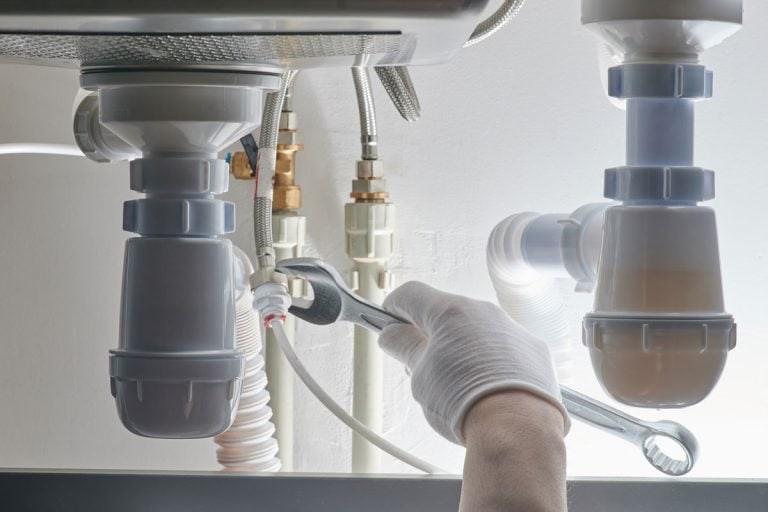 Hand with wrench tighten screw on pipe, How To Tighten Kitchen Faucet Nut Under Sink