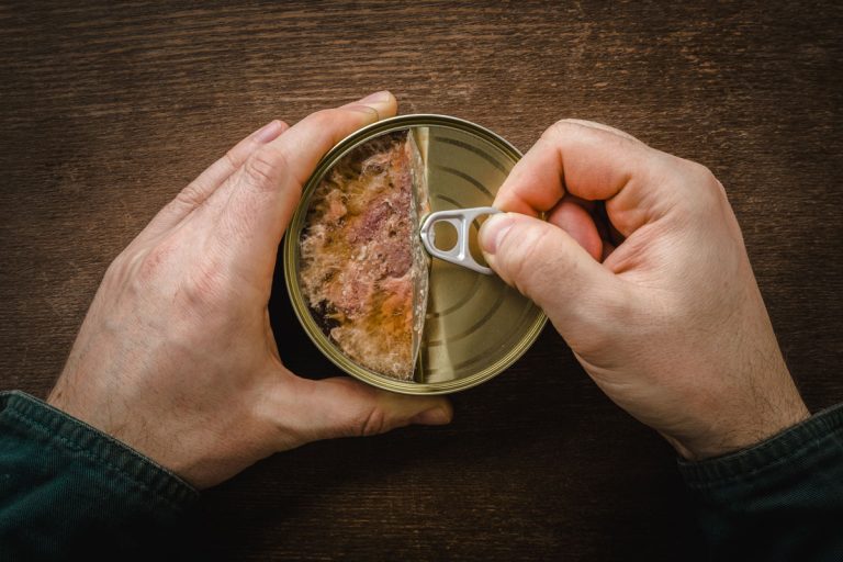 Man hands opening tin can with chicken meat on dark wooden table background, Is Canned Chicken Always Pre-Cooked?
