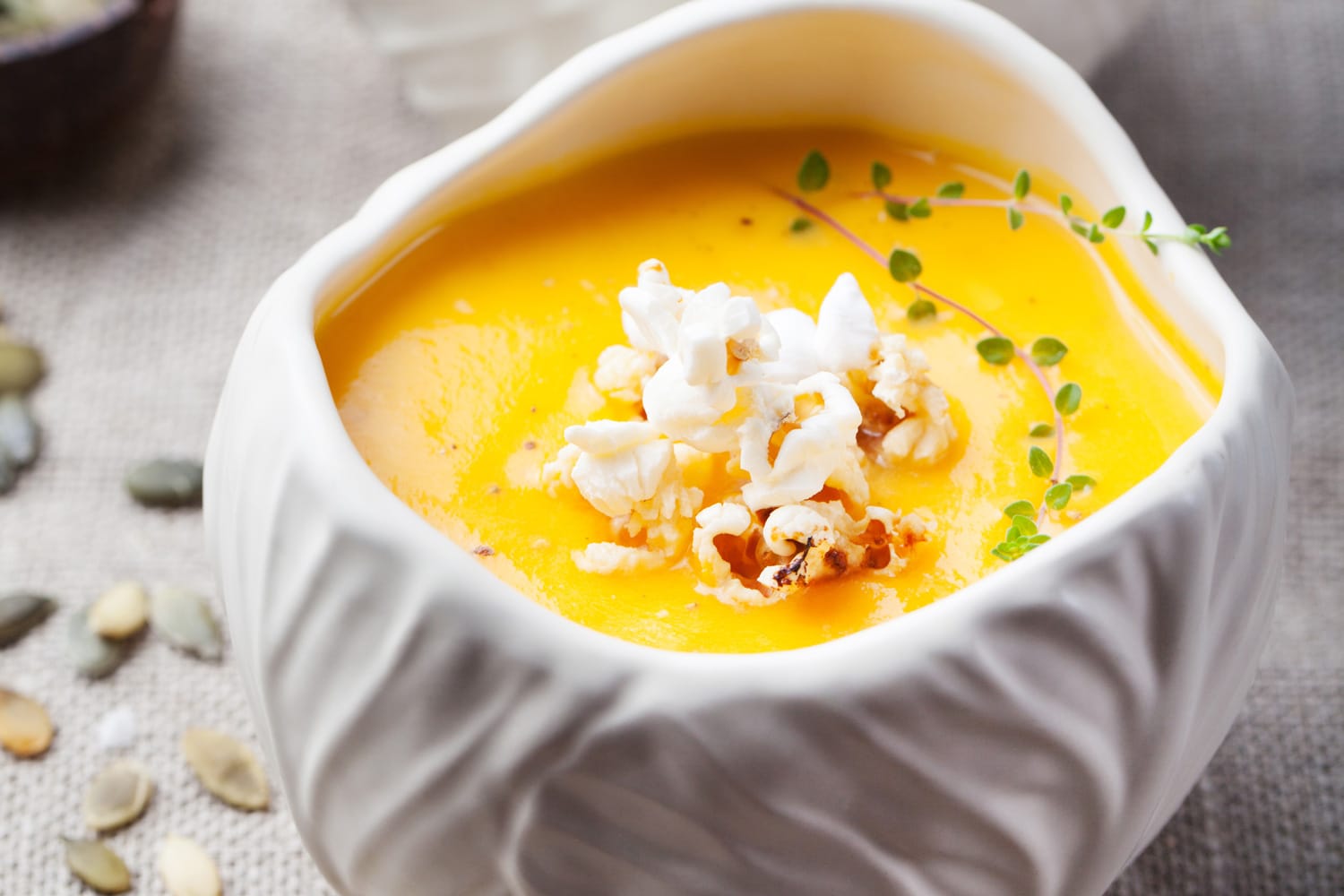 南瓜、玉米汤咸爆米花在一个白色的陶瓷碗一个木制背景”width=