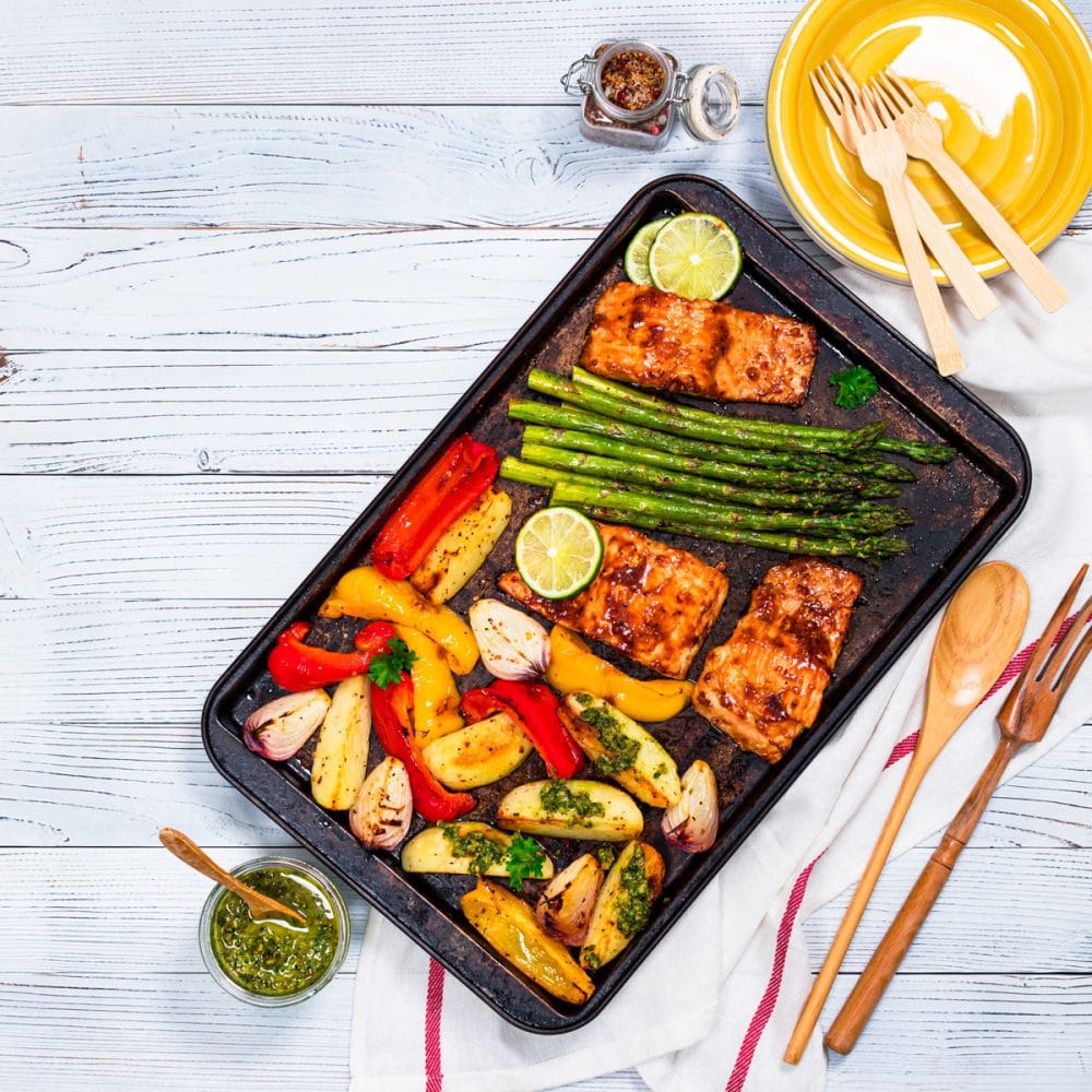一个黑色的烤盘，里面有烤好的欧芹，西红柿和玉米