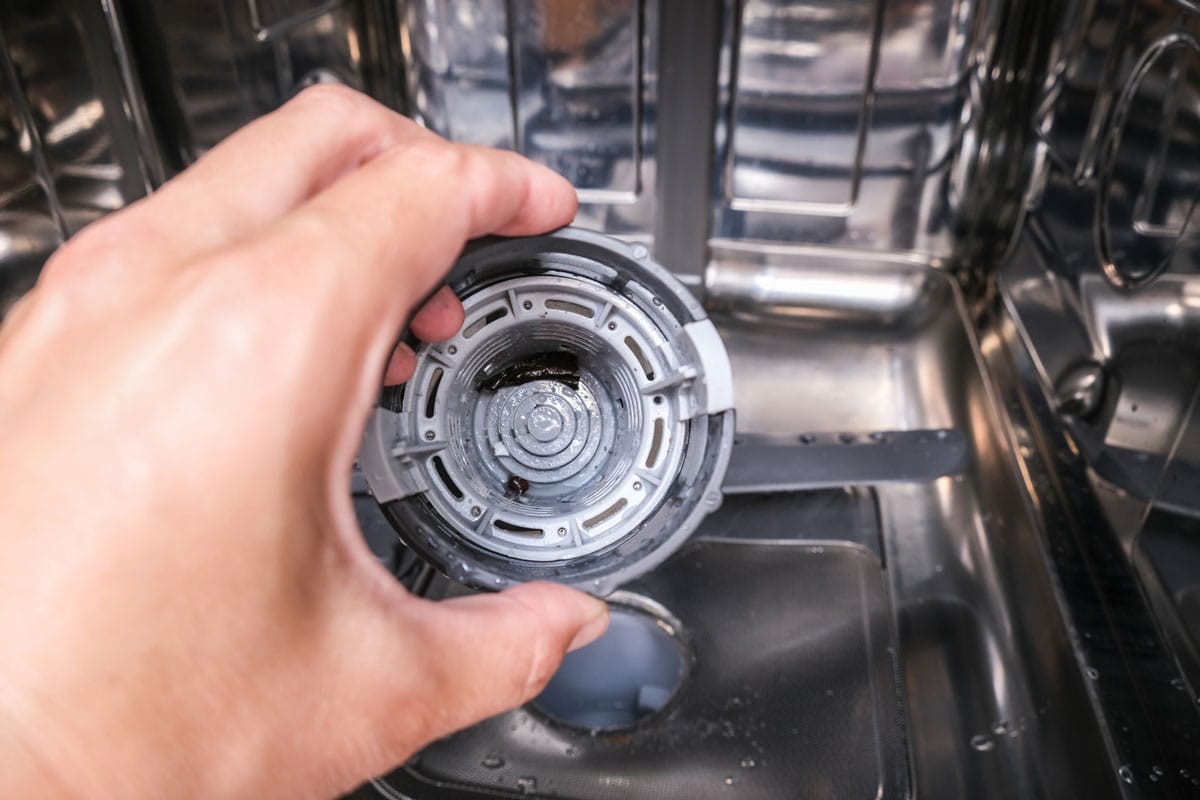 一只手拿出洗碗机的过滤器来清洗