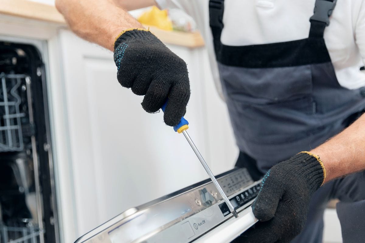 近距离维修和安装洗碗机，男性工人穿着制服，拿着工具。