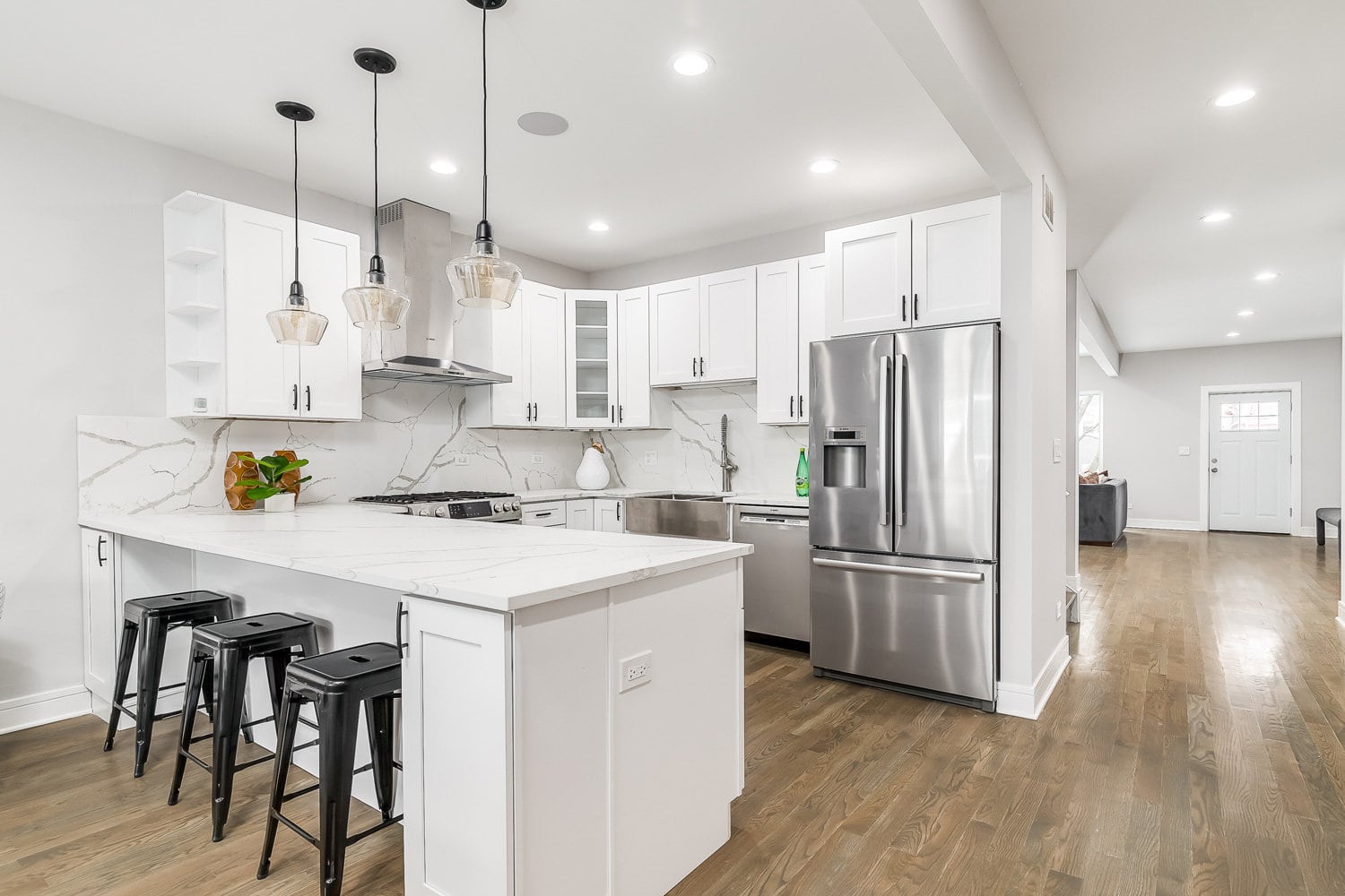 一个全新的、现代的全白色厨房，天花板上挂着黑色的雷电竞官网网址灯，吧台上方放着黑色的吧台凳，作为用餐区。亮着灯。