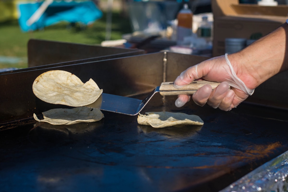 一只肤色浅的手戴着准备食物的手套，在热煎锅上煎玉米饼