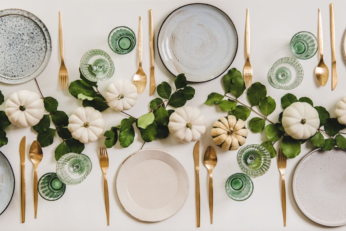 秋季餐桌设置庆祝感恩节或朋友节，家庭聚会或聚会。平铺的盘子，餐具，玻璃器皿，南瓜和树叶在纯白色的桌子背景，俯视图”width=