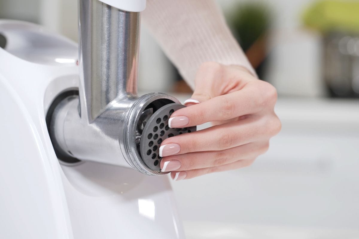 女性手设置切盘在绞肉机提供优质的肉末从所有类型的肉。电动绞肉机每分钟可绞碎肉末，制作香肠，捣碎浆果，榨果汁。