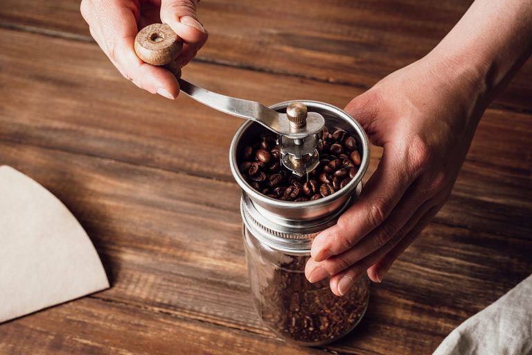 Grinding coffee beans in a manual coffee grinder on a wooden table. Can You Grind Salt In A Coffee Grinder Or Food Processor?