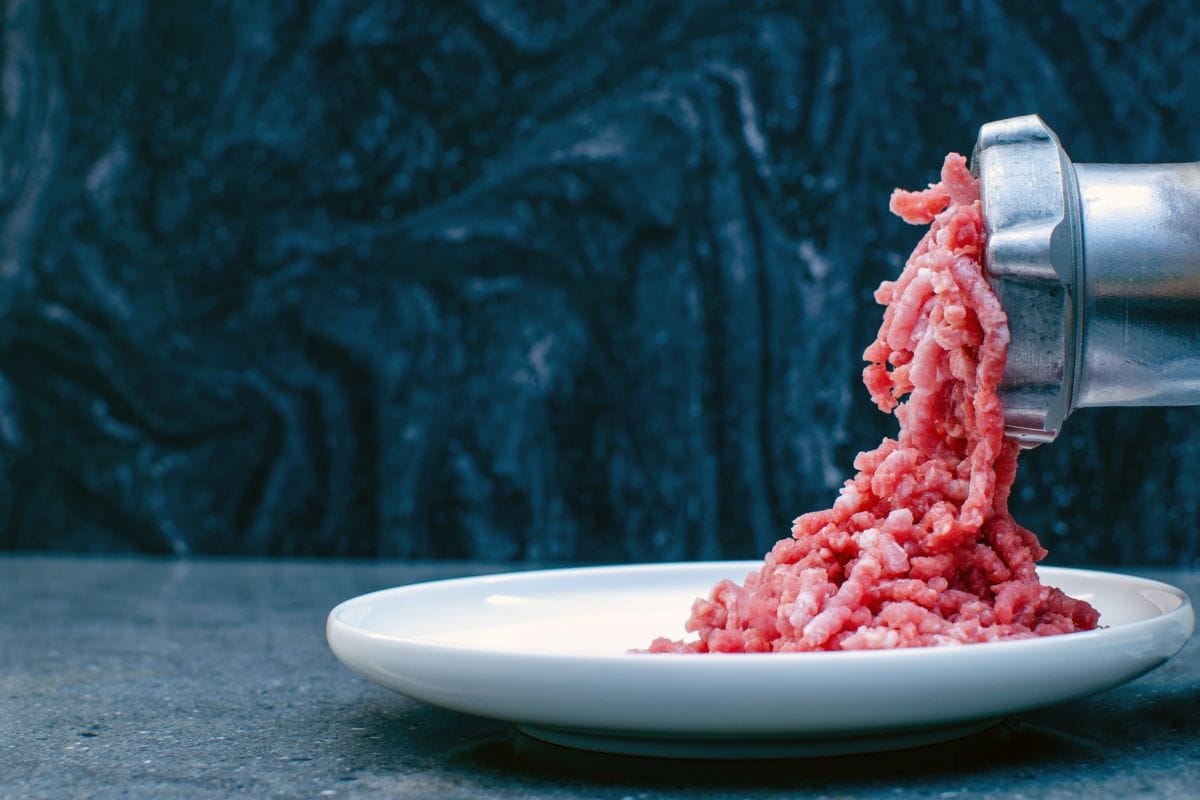 在金属手动绞肉机上研磨新鲜的红肉，特写在带有复制空间的砖墙背景上