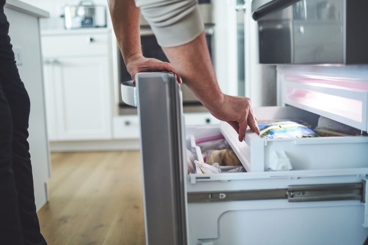 无法辨认的男性在一个打开冰箱冷冻室抽屉