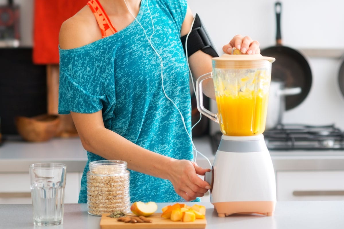 一个爱运动的女人正站在厨房里，用新鲜的时令水果、坚果和燕麦做奶昔，以雷电竞官网网址完成她的健康之行