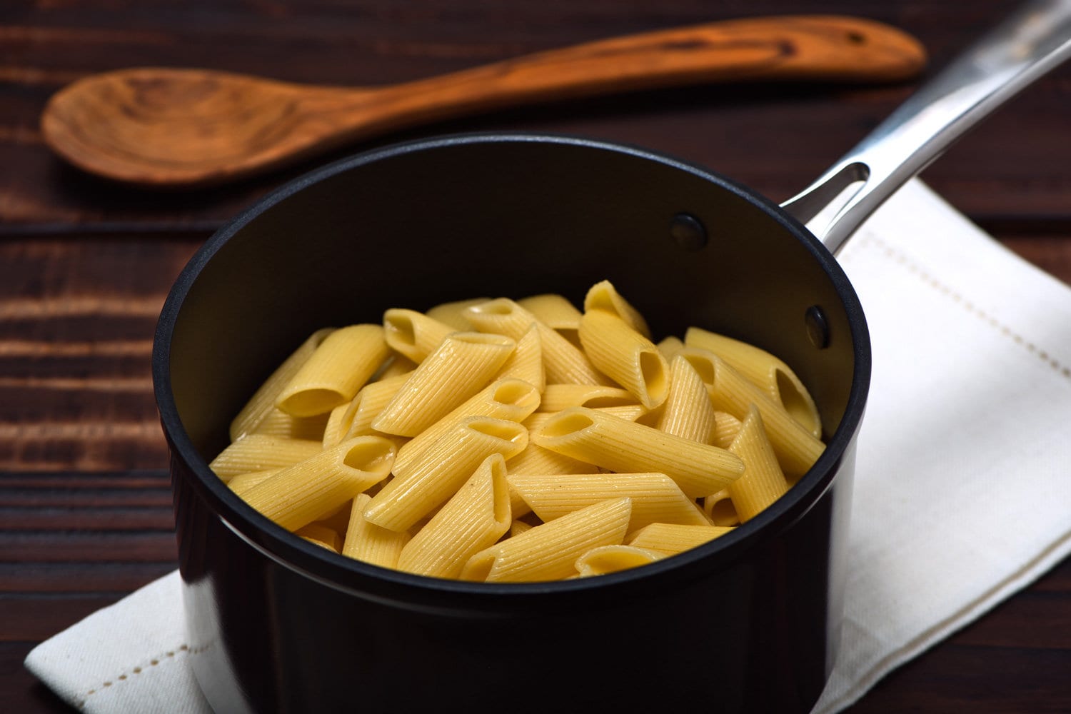 煮熟的面条(Penne Rigate)在一个专业的阳极氧化铝不粘锅上，餐巾在一个老式的木制表面。