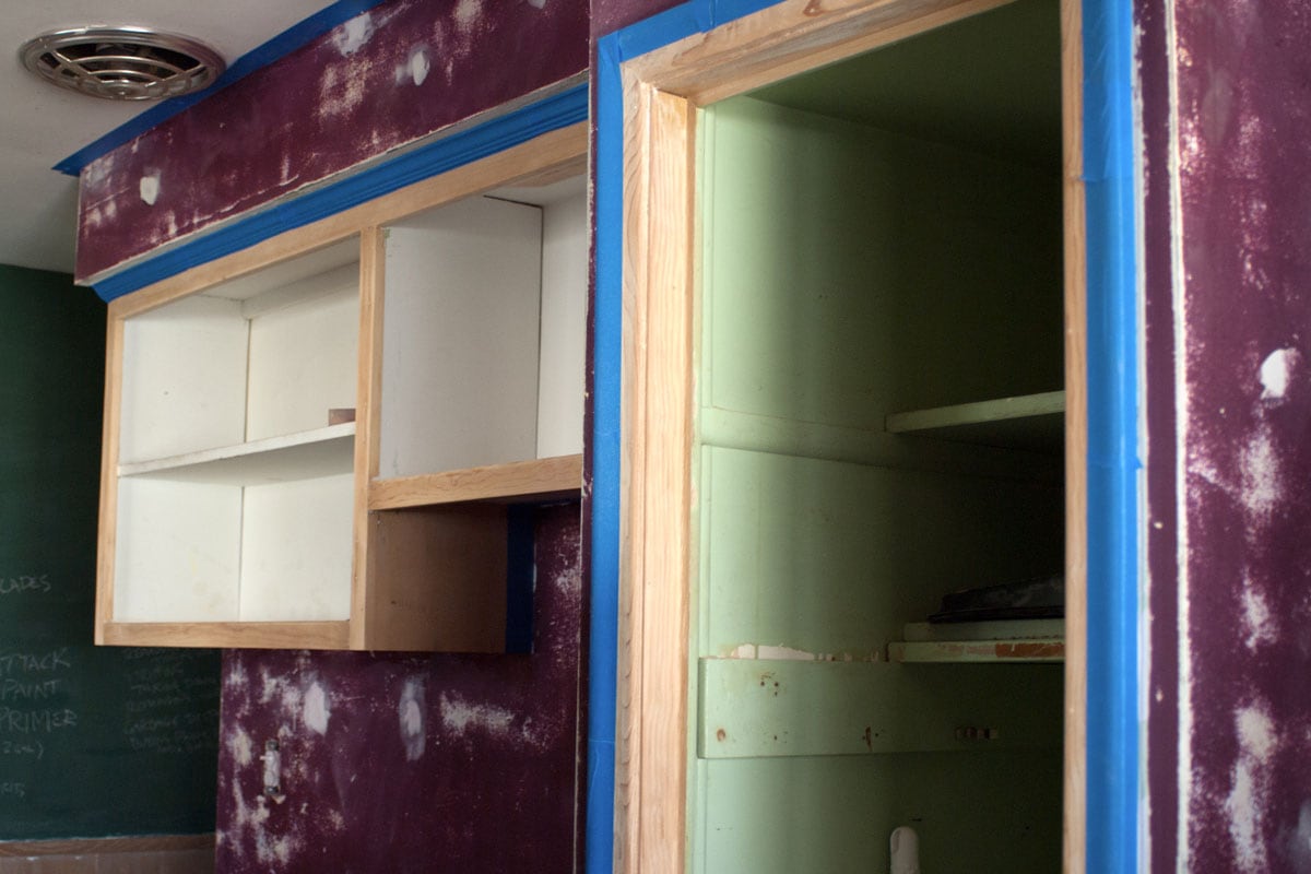 室内用胶带封好，准备粉刷，紫色的墙壁用砂纸打磨并打了补丁，空的橡木橱柜，以及一间没有门的储藏室”width=