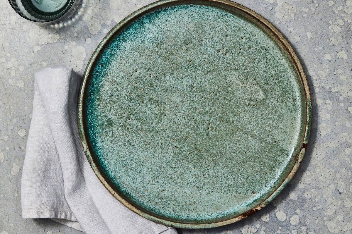 静物摄影家用亚麻布的绿色陶瓷板、水玻璃、胡椒研磨机和一个