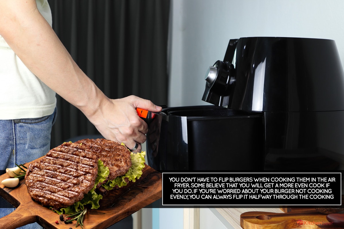 男人的右手拿着托盘的黑色深空气炸锅或无油炸锅设备在木桌上的白色的厨房(空气炸锅)在与家人共进午餐,你需要在空气炸锅汉堡包吗?雷电竞官网网址