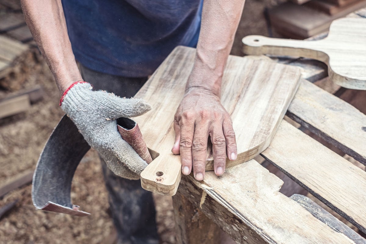 Carpenter sanding wood with sandpaper at workshop in wooden cutting board project or woodworking carpentry