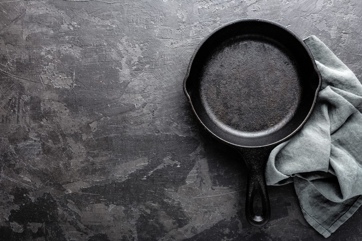 Empty cast iron frying pan on dark grey culinary background, view from above - How To Strip Cast Iron Without Oven Cleaner