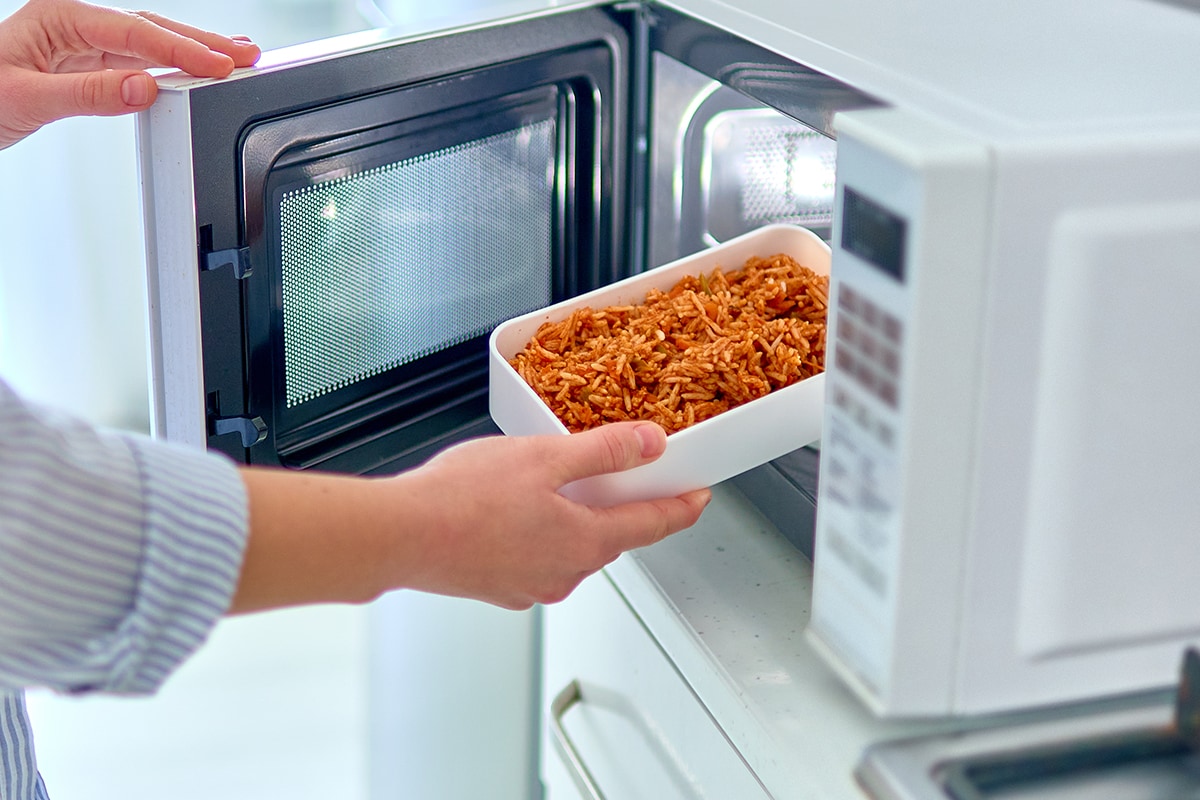 Hands warming up a container of food in the modern microwave oven