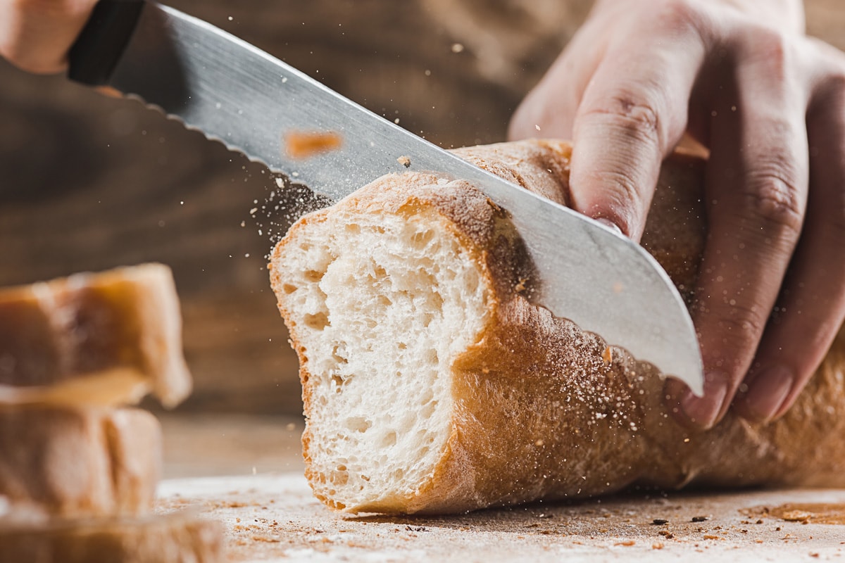 Whole grain bread put on kitchen wood plate with a chef holding gold knife for cut.