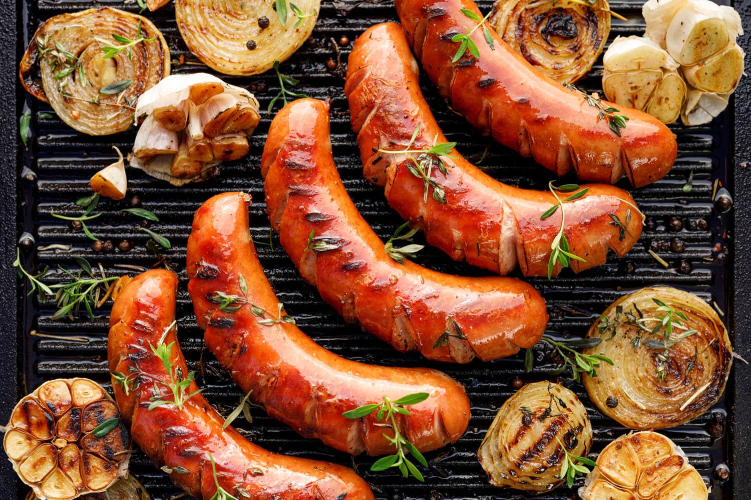 Grilled sausage with the addition of herbs and vegetables on the grill plate, outdoors. Grilling food, bbq, barbecue