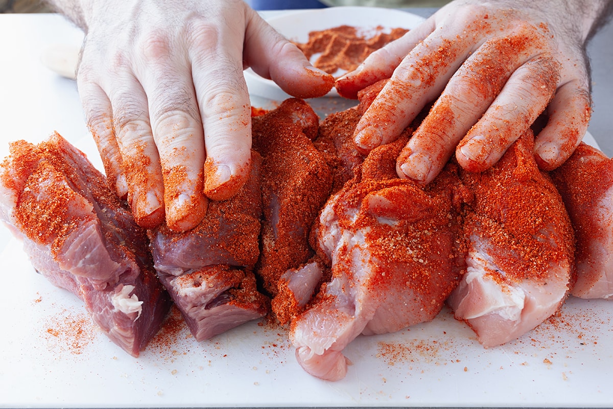 Male hands rubbing dry rub spices in pork tenderloin pieces